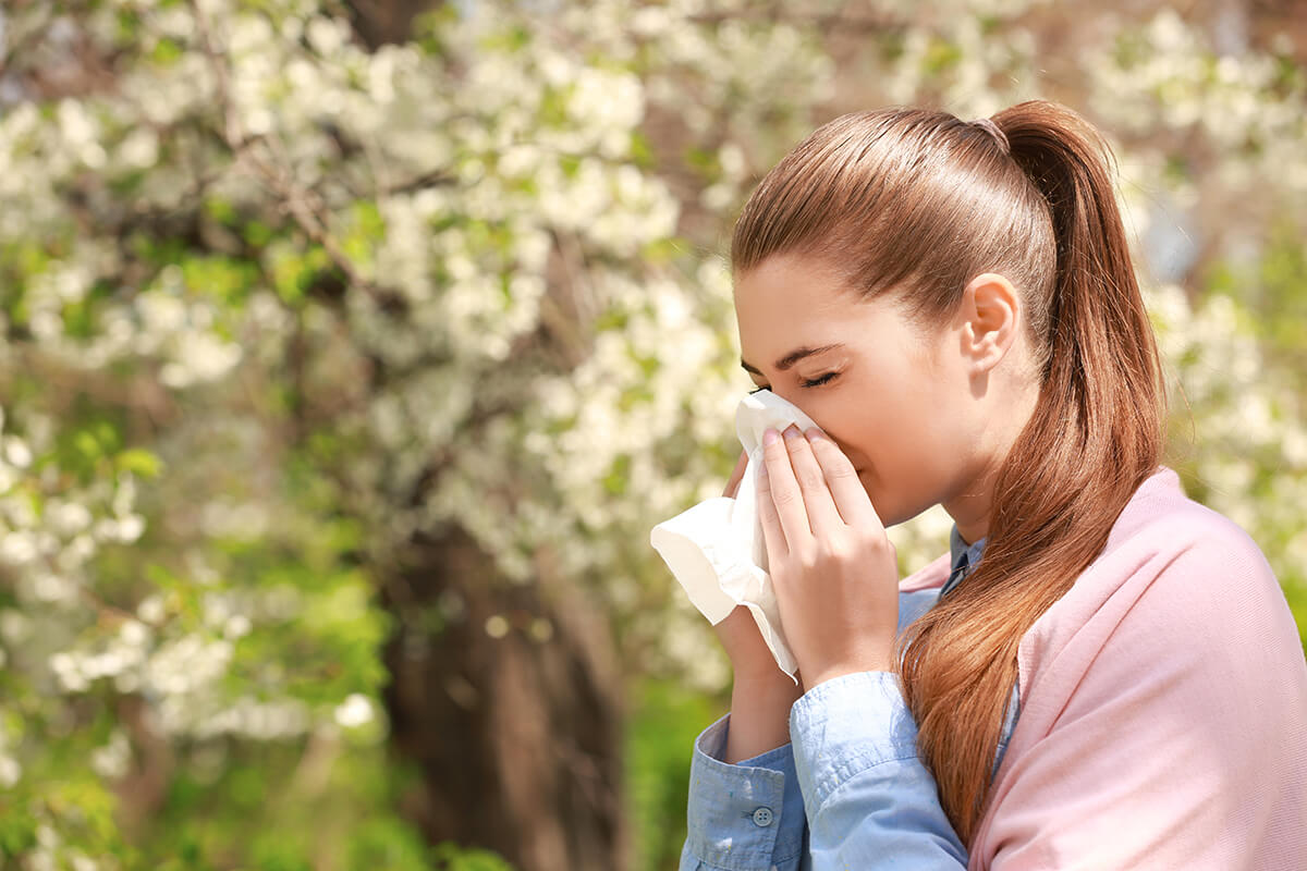 Sneezing Young Girl With Nose Wipe Among Blooming Trees