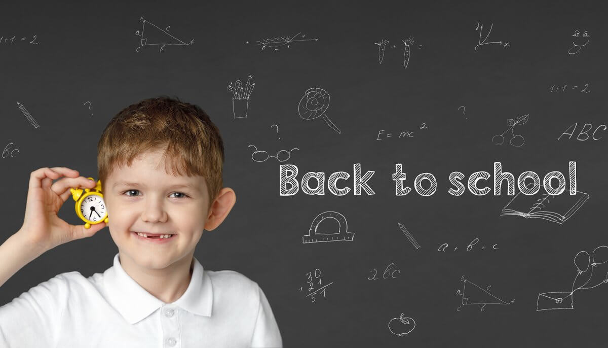Happy child with small clock near a school board with inscriptions. Back to school, education concept.