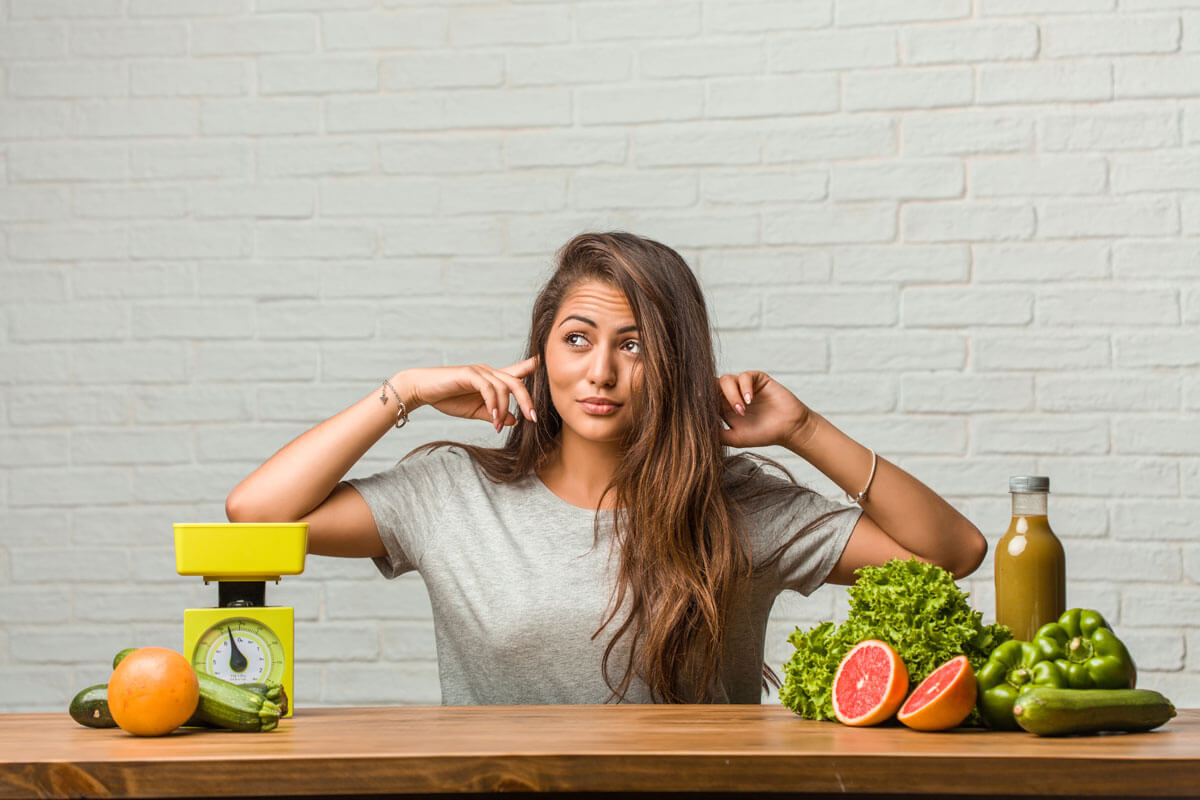 woman plugging her ears while sitting next to scale and healthy food